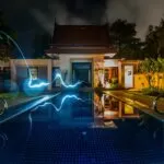 reflection of blue light crossing above pool near house during nighttime